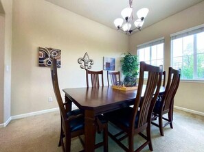 A dining room with a wooden table and chairs, a chandelier, and artwork on the walls.