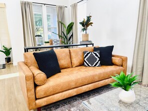 A tan leather sofa with patterned cushions, a glass coffee table, and a potted plant.