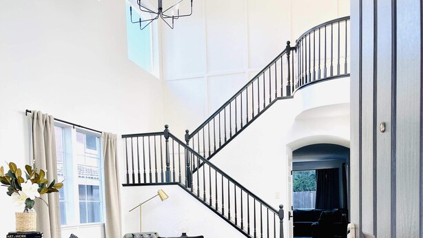 A spacious living room with a staircase, a leather sofa, a bookshelf, and a chandelier. - Huge Home near Old Folsom, Pet & Family Friendly (Folsom)