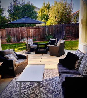 Un patio al aire libre con un conjunto de sofá, una mesa de centro y una sombrilla.