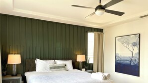A bedroom with a bed, two bedside tables, a ceiling fan, a window with curtains, and a painting on the wall.
