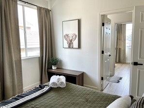 A hotel room with a bed, a bedside table with towels, a potted plant, and a framed picture on the wall. - Remodeled 4BR near Historic Folsom · Walk to Shops · Pets OK (Folsom)