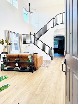Un salon spacieux avec un escalier, un canapé en cuir, une bibliothèque et un lustre.