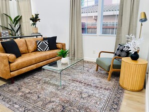 A living room with a brown leather sofa, a glass coffee table, a patterned rug, a green armchair, and a small side table with a vase. - Remodeled 4BR near Historic Folsom · Walk to Shops · Pets OK (Folsom)