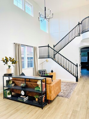 Ein geräumiges Wohnzimmer mit hoher Decke, einer schwarzen Treppe und einem modernen Kronleuchter.