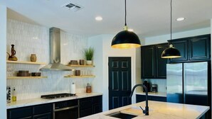 A modern kitchen with dark cabinetry, a marble island, pendant lighting, and a stainless steel range hood. - Huge Home near Old Folsom, Pet & Family Friendly (Folsom)