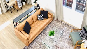 Een ruime woonkamer met een bruine bank, een glazen salontafel en een kroonluchter.