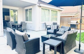 Een terras buiten met rieten meubilair, een barbecue en een overdekt gedeelte.