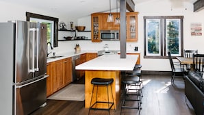 Eine moderne Küche mit einer großen Kochinsel, Edelstahlgeräten, Holzschränken und einem Essbereich mit einer schwarzen Ledersofa.
