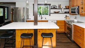 Eine moderne Küche mit einer großen Kochinsel, Holzschränken, Edelstahlgeräten und Barhocker.