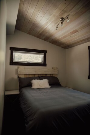 Une chambre avec un plafond en bois, une fenêtre au-dessus du lit et une tête de lit.