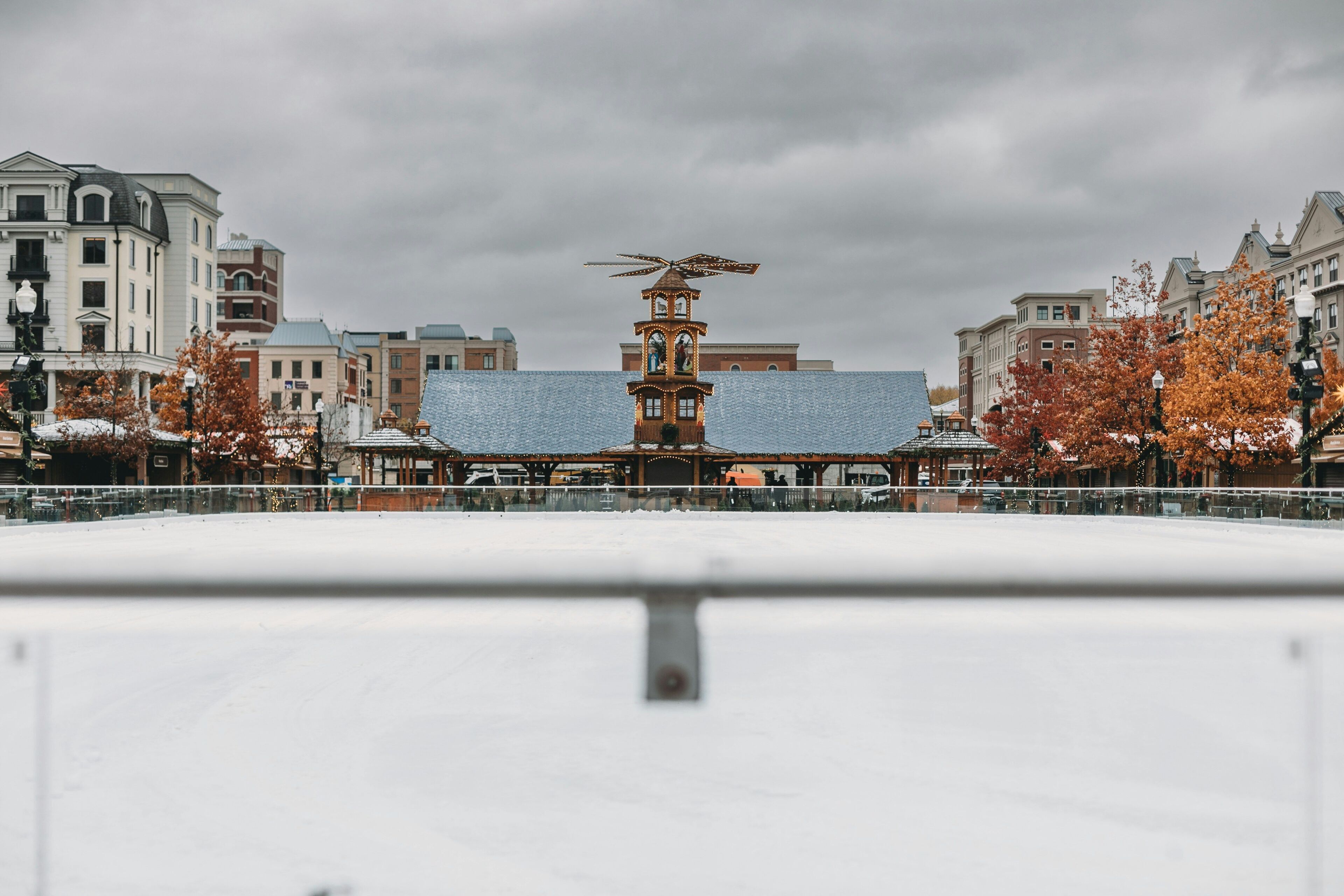 A snow-covered plaza with a central building featuring a clock tower and a distinctive roof ornament.
