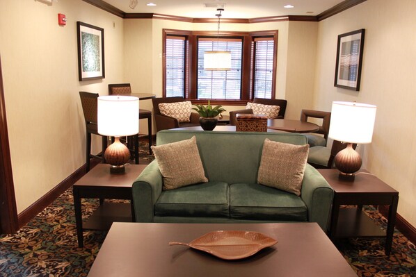 A hotel lobby with a green sofa, two lamps, a table with a decorative leaf, and a patterned carpet.