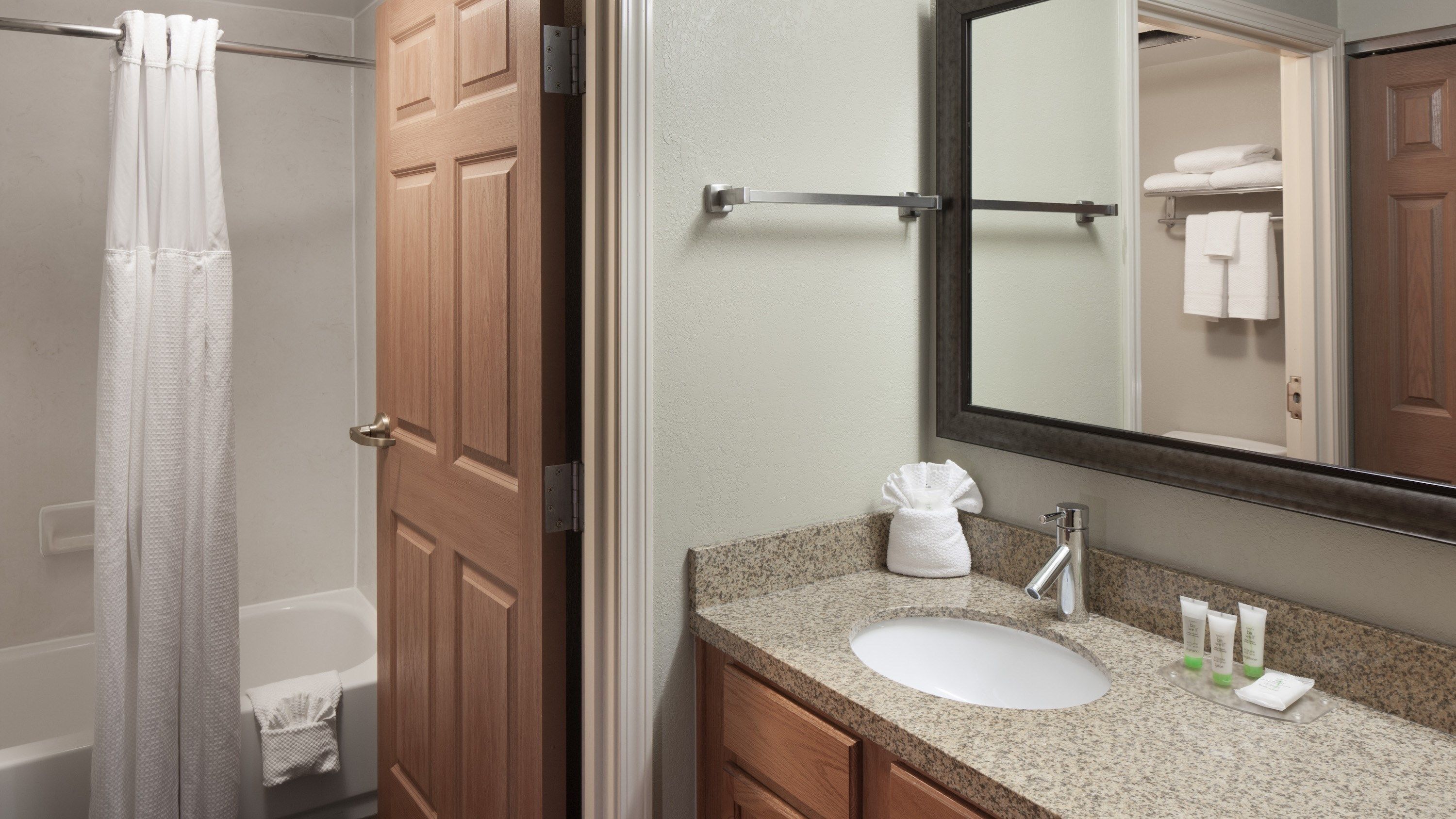 A bathroom with a wooden door, a white sink, a mirror, and a towel rack.