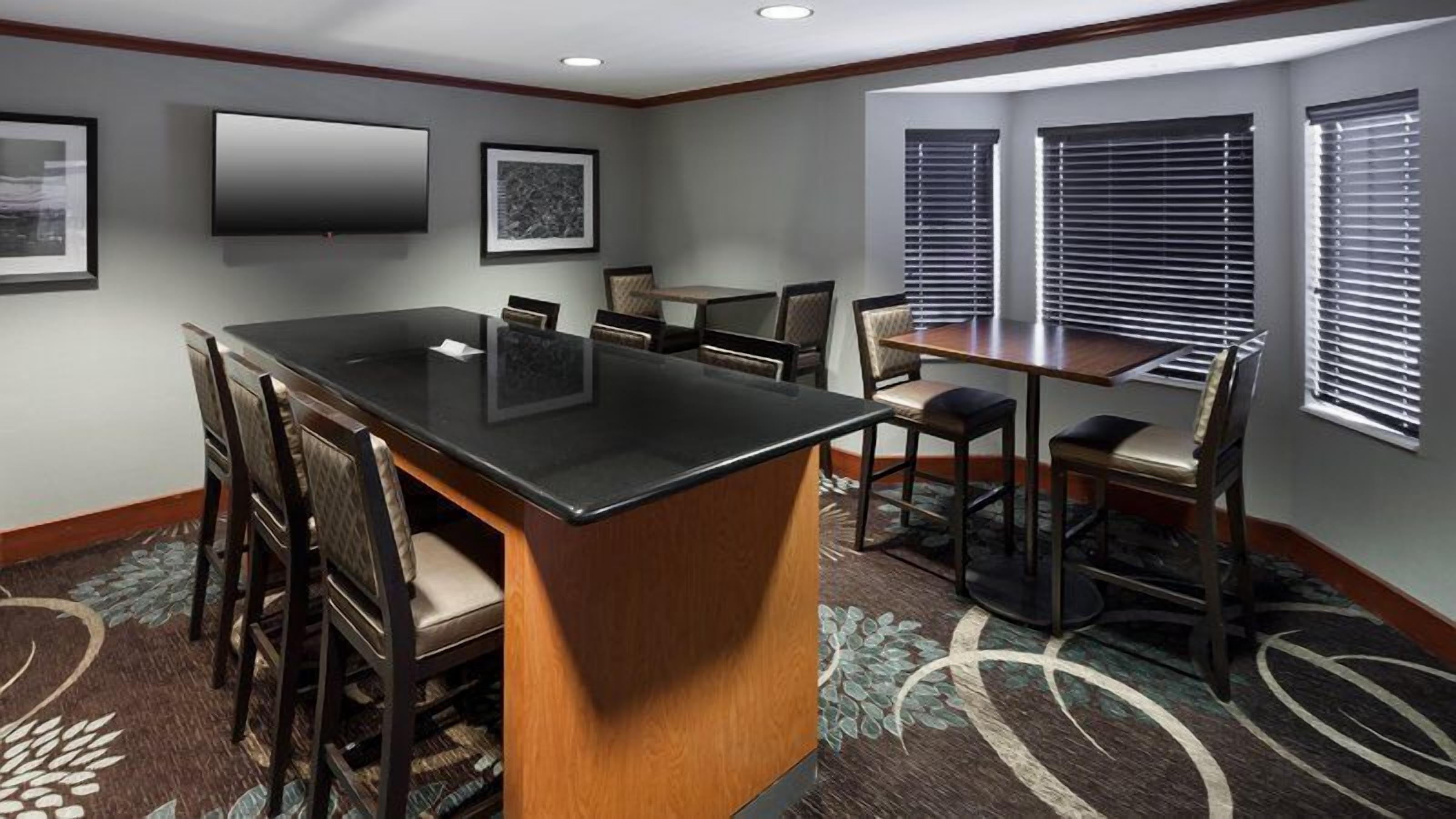 A conference room with a central table, surrounding chairs, a smaller table, and a window with blinds.