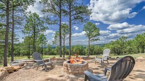 An outdoor seating area with Adirondack chairs around a stone fire pit, surrounded by trees and a clear sky. - Log Cabin with Million Dollar View! “The Time Out” Secluded property (tuskahoma)