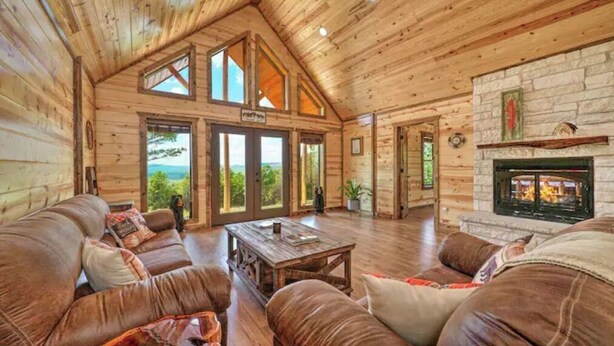 A log cabin interior with a large living area, a fireplace, and a view through the glass doors. - Log Cabin with Million Dollar View! “The Time Out” Secluded property (tuskahoma)