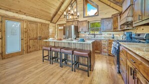 A rustic kitchen with wooden cabinets, a large island with bar stools, and a hanging light fixture. - Log Cabin with Million Dollar View! “The Time Out” Secluded property (tuskahoma)