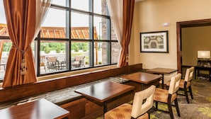 Une chambre d’hôtel dotée d’une grande fenêtre, d’un banc en bois et d’un coin repas avec des tables et des chaises.