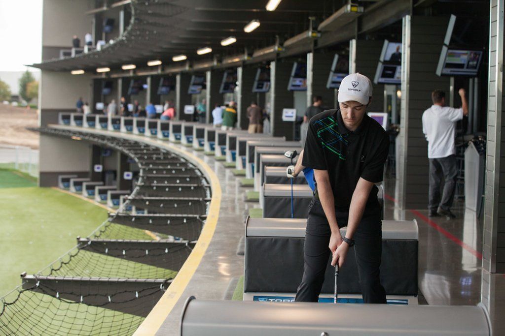 Un campo de golf con un jugador a punto de hacer putt, una zona delimitada por una red y un graderío.