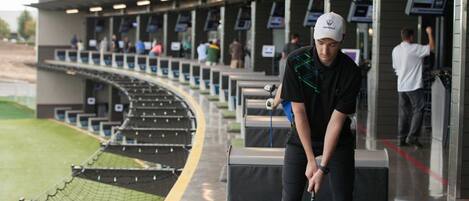 Un campo de golf con un jugador a punto de hacer putt, una zona delimitada por una red y un graderío.