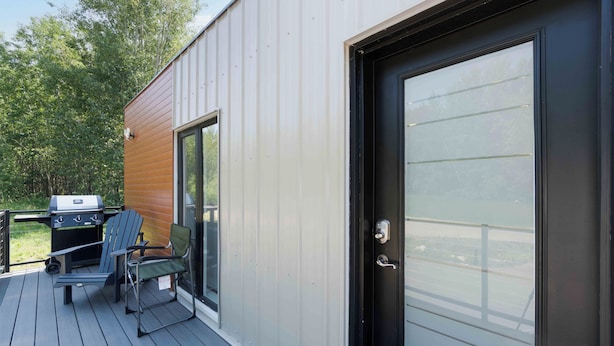 A deck with a grill and chairs, a sliding glass door, and a view of the outdoors. - Beautiful Modern home peaceful location (Alberta Beach)