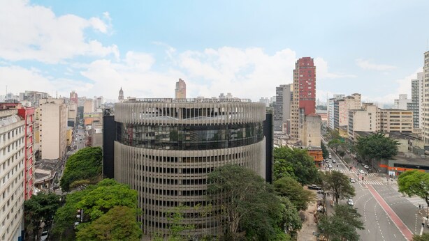 A high-rise building with a unique cylindrical design, surrounded by other tall buildings and trees.