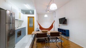 A modern kitchen with a stainless steel refrigerator, a wooden dining table with two chairs, and a blue console table with a TV.