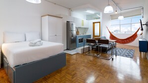 A modern room with a bed, kitchenette, and a hammock.