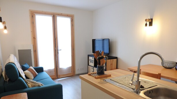 Una sala de estar moderna con un sofá azul, una mesa de comedor de madera y una cocina con lavamanos y encimera.