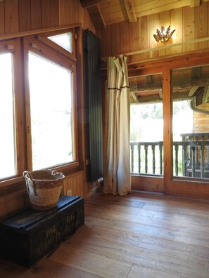 L’intérieur d’un chalet en bois, avec de grandes fenêtres, un plancher en bois, un panier et une valise ancienne.