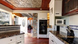 Cocina con armarios blancos, una pared de acento de piedra, un microondas y un bloque de cuchillos.