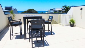 A patio with a table and chairs, a potted plant, and a view of the ocean. - 3 Bedroom Central Beachside Kingscliff Apartment with Pool (Kingscliff)