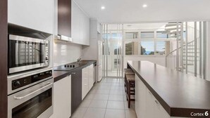 A modern kitchen with a built-in oven, microwave, and a large island with seating. - 3 Bedroom Central Beachside Kingscliff Apartment with Pool (Kingscliff)