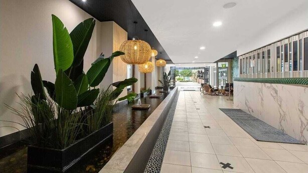 A modern hotel lobby with a long corridor, potted plants, and hanging spherical light fixtures. - 3 Bedroom Central Beachside Kingscliff Apartment with Pool (Kingscliff)