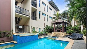A swimming pool area with a gazebo, lounge chairs, and a building with balconies. - 3 Bedroom Central Beachside Kingscliff Apartment with Pool (Kingscliff)