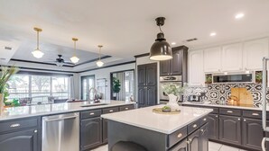 A modern kitchen with dark cabinets, a central island, and pendant lighting. - Spacious Group Retreat | 3 Kings | Sleeps 25 (Ft. Worth)