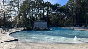 A swimming pool with a water fountain, surrounded by lounge chairs and a paved deck.