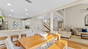A spacious living area with a wooden dining table, light-colored sofas, and a staircase leading to an upper level.