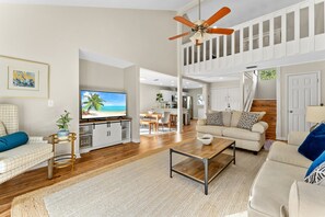 Un amplio espacio de sala con televisor, sofá, mesa de centro y ventilador de techo.