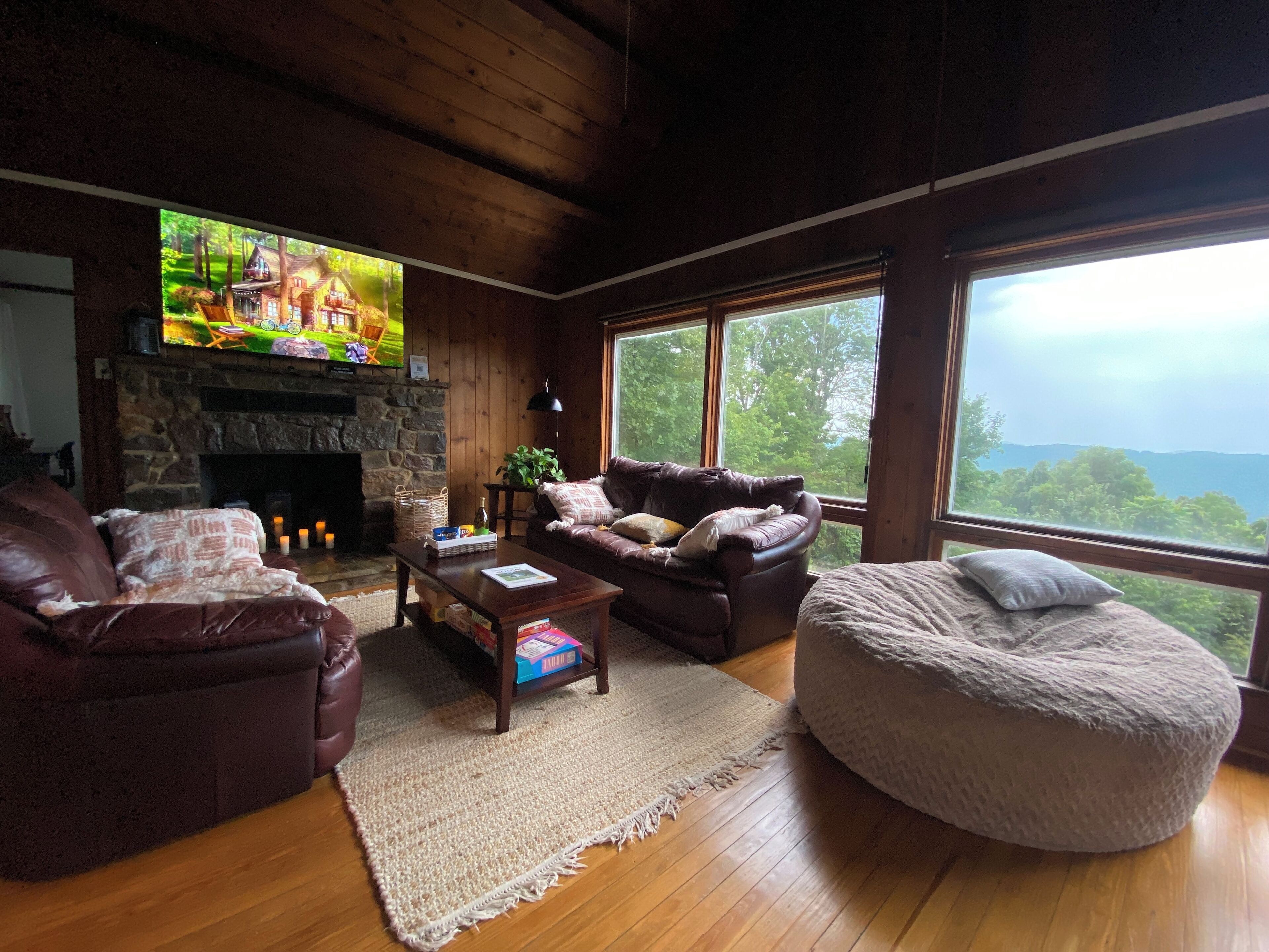 A cozy living room with a stone fireplace, leather sofas, a large TV, and a view of the outdoors.