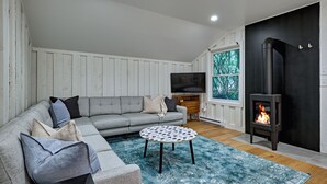 Un salon chaleureux avec un canapé gris, une table basse ronde, un téléviseur et un poêle à bois.