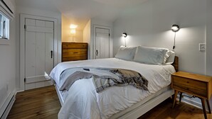 Une chambre à coucher avec un grand lit, deux tables de chevet, une commode en bois et deux lampes fixées au mur.