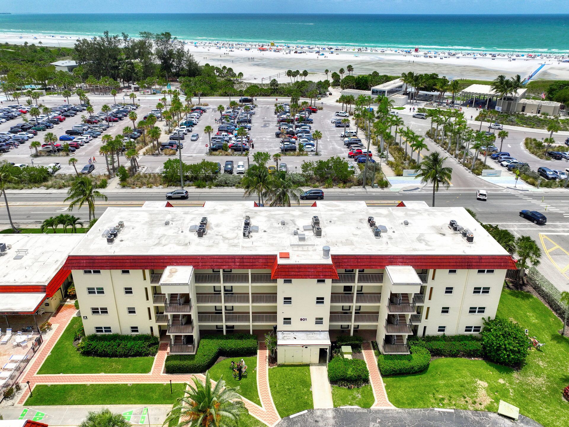 Un hôtel à plusieurs étages, avec un toit rouge, un parking et une vue sur la plage.