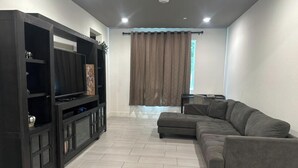 Un salón con un sofá modular, un mueble de entretenimiento de madera oscura y un ventanal con cortinas.