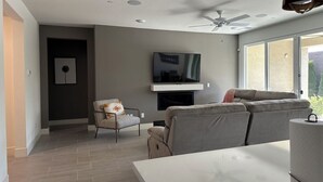 Una sala de estar moderna con un televisor de pantalla plana, un sofá, una silla y un ventilador de techo.