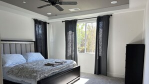 Un dormitorio con una cama, un ventilador de techo, una ventana con cortinas y un armario.