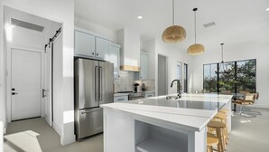 Et moderne køkken med en central ø, rustfrie hårde hvidevarer og et spiseområde med træborde.
