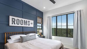 Et soveværelse med en stor seng, et natbord, en lampe, et vindue med gardiner og et skilt på væggen med teksten "ROOMS".