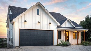 Et moderne hus i et plan med stor garage, overdækket veranda og mindre tilhørende garage.